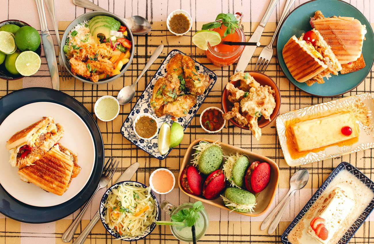 Gedekte tafel met sandwiches, salades, desserts en drankjes, kleurrijk gebak en diverse sauzen.