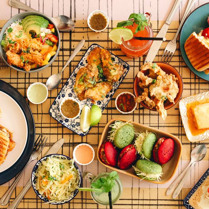 Gedekte tafel met sandwiches, salades, desserts en drankjes, kleurrijk gebak en diverse sauzen.