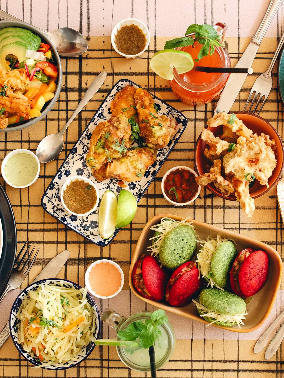 Gedekte tafel met sandwiches, salades, desserts en drankjes, kleurrijk gebak en diverse sauzen.