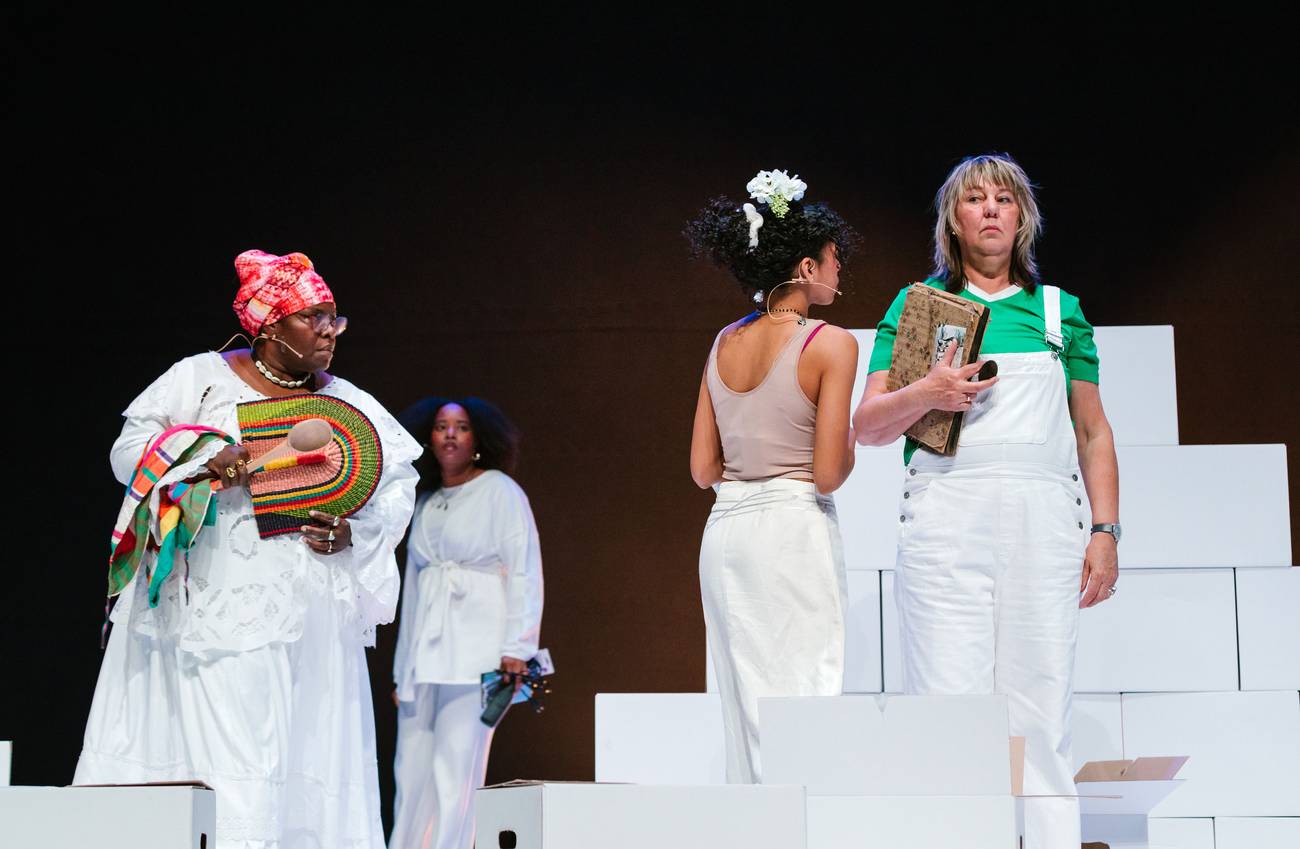 Vier vrouwen, gekleed in het wit, van verschillende afkomsten op een podium tijdens een voorstelling