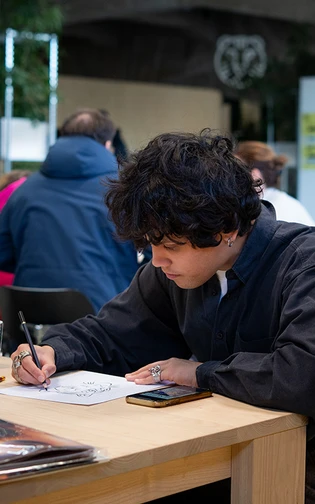 een persoon zit aan een tafel geconcentreerd een tekening te maken