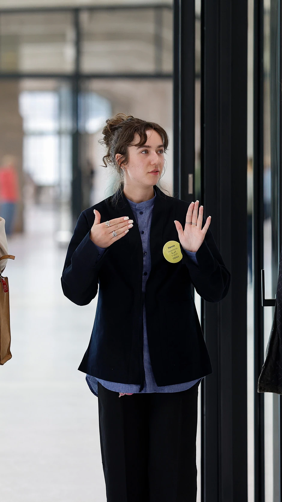 A group of four people stands in discussion indoors. One person gestures while talking. T