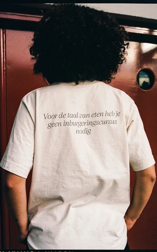 Persoon van op de achterkant gezien draagt shirt met de tekst: 'voor de taal van eten heb je geen in