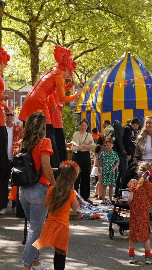 A lively street festival features people dressed in orange amidst colorful tents.