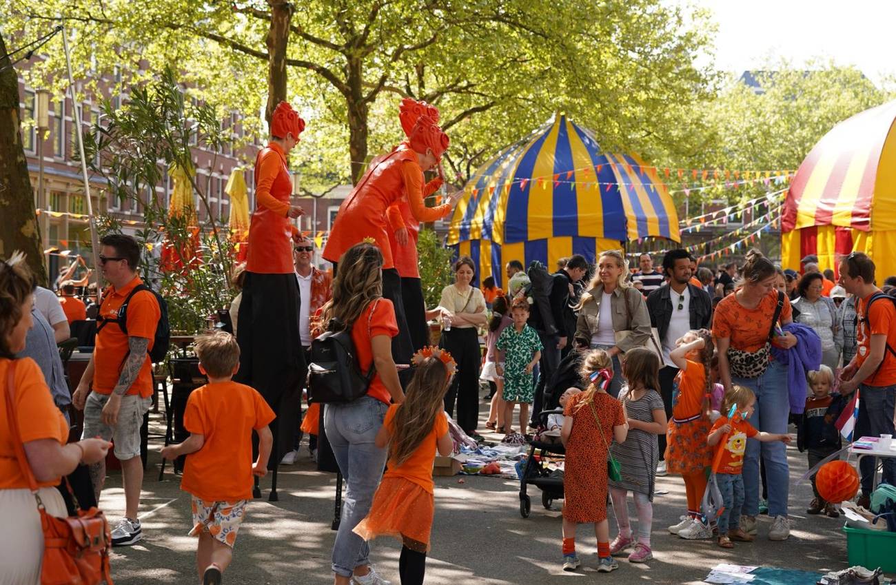 A lively street festival features people dressed in orange amidst colorful tents.