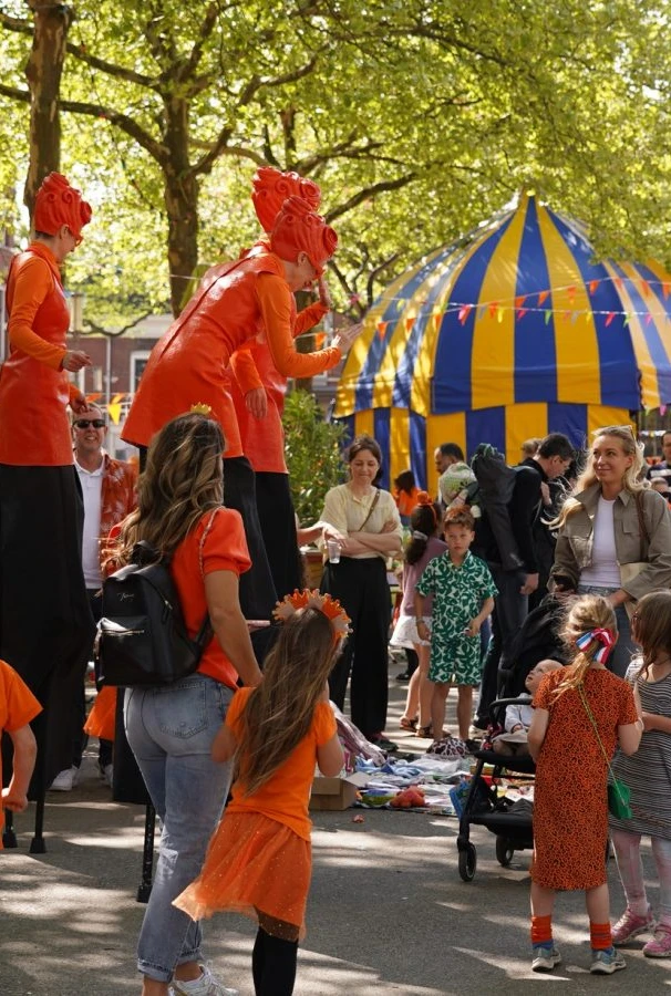 A lively street festival features people dressed in orange amidst colorful tents.