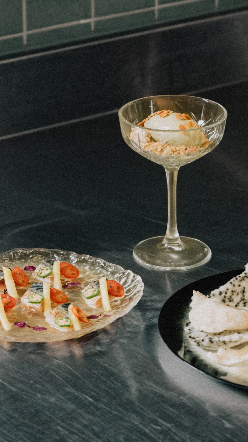 Elegant dish trio on a stainless-steel counter: mackerel, dessert in a glass, and tartar.
