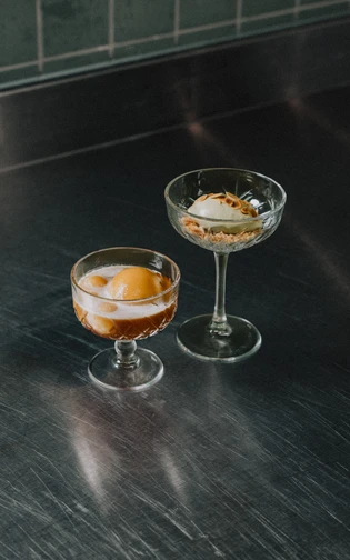 Two elegant dessert glasses on a stainless steel surface.