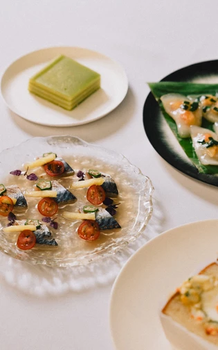 A stylish food spread: a plate of sashimi with tomatoes and herbs, dumplings, and green desserts.