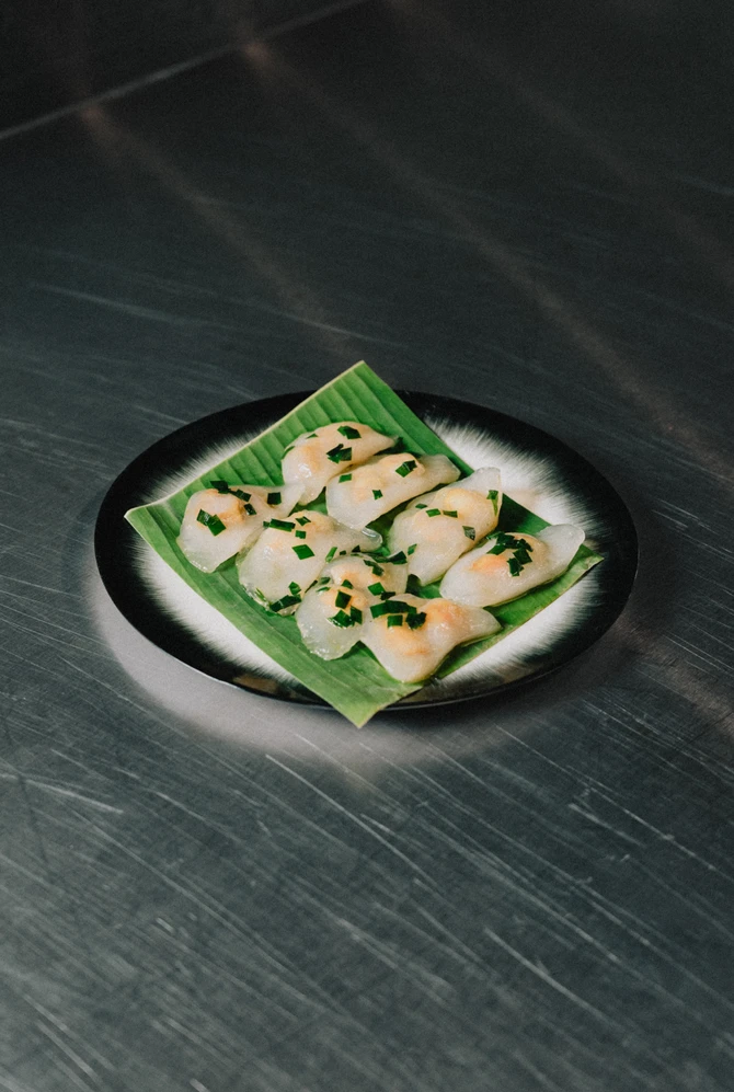 A plate of tapioca shrimp dumplings garnished with chopped chives sits on a green leaf.