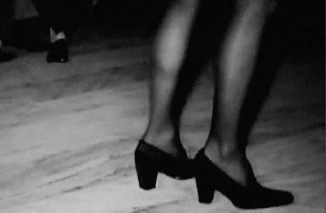 zwart-wit still uit een film, waarop afgesneden twee vrouwelijke benen te zien zijn.