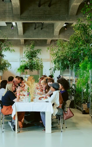 lange tafel omringt door hoge plantenbakken. de tafel is sfeervol gedekt, en aan tafel zitten mensen
